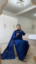 Woman in royal blue Farah shalwar with lace detailing, seated in a stylish room with modern decor.