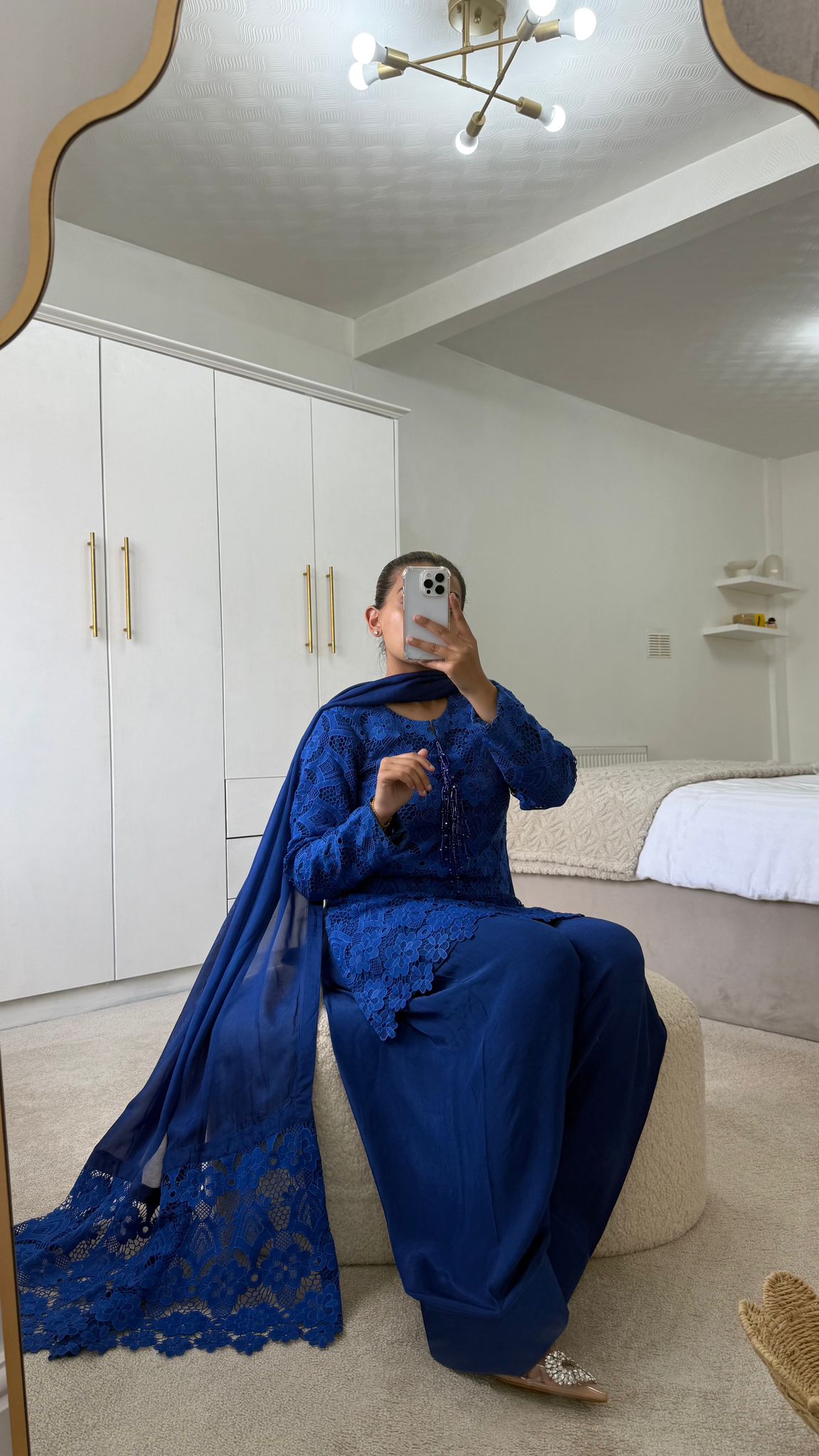 Woman in royal blue Farah shalwar with lace detailing, seated in a stylish room with modern decor.